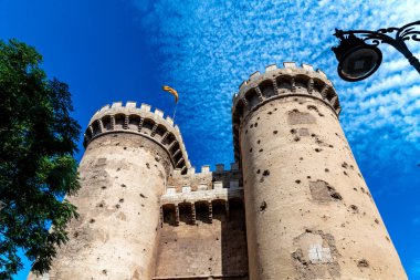 Torres de Serranos kuleleri, hava durumu, kurşun izleri ve mavi gökyüzünde Valencia bayrağı.