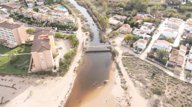 Denia, Alicante - İspanya - 11-13-2024: Kumlu plajlar arasında akan küçük bir köprüyle sakin bir nehrin havadan görünüşü.