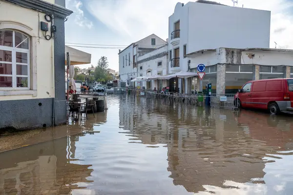 Tavira, Algarve - Portekiz - 09-18-2024: Kafe masaları, kırmızı minibüs, beyaz binalar ve bulutlu gökyüzü sakin bir manzara yaratıyor.