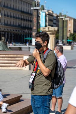 Saragossa, Saragossa - İspanya - 09-10-2021: Zaragoza, İspanya 'da maskeli bir tur rehberi, yeşil gömlek ve kimlik kartı giyerken bir dönüm noktasını açıklıyor.
