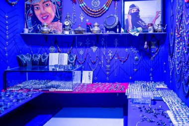 Agadir, Souss-Massa - Morocco - 08-03-2024: A shop filled with Moroccan jewelry, artifacts, blue walls, chains, amulets, vases, teapots, and portraits of women in traditional clothes. clipart