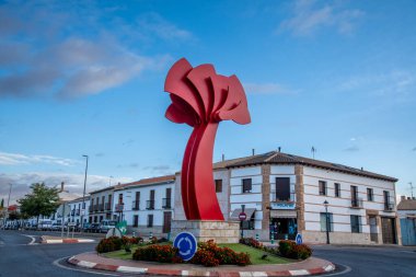 Almagro, Ciudad Real - İspanya - 10-09-2024: The Flor de Calatrava, çiçeklerle ve binalarla çevrili bir trafik çemberinde duran, stilize edilmiş bir çiçeği andıran kırmızı modern bir heykeldir..