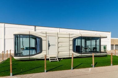 Almancil, Algarve - Portekiz - 09-19-2024: Mavi battaniyeli, beyaz yastıklı, komodinli ve minimalist tasarımı yansıtan eğri camlı modern modüler yatak odası.