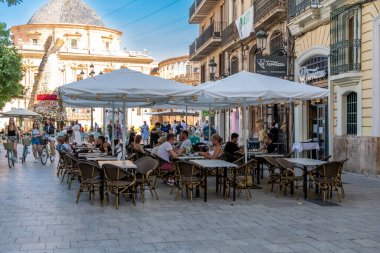 Valencia, Valencia - İspanya - 09-08-2021: Beyaz şemsiyeli sokak kafesi, dinlenen insanlar, tarihi binalar ve büyük bir kubbe yapısı.