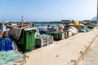 La Linea de la Concepcion, Cadiz - Spain - 08-28-2024: Harbor area with fishing equipment: green bins, ropes, nets, and boxes on concrete floor. Boats and harbor structures are in the background under a clear sky. clipart