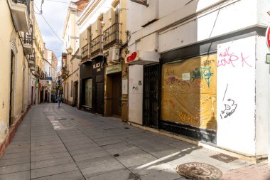 Merida, Badajoz - İspanya - 10-07-2024: Merida 'daki dar bir kaldırım taşı caddesinde sarı ve beyaz binalar, balkonlar, dükkanlar ve graffiti yer alıyor..
