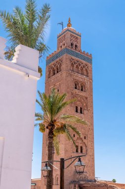 Marakeş 'te kırmızı taştan yapılmış Koutoubia Camii minaresi beyaz bir bina, dekoratif elementler, palmiyeler, altın ve mavi süsler.