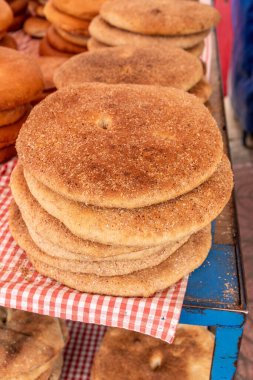 Bir yığın yuvarlak, altın kahverengi somun mavi bir masanın üzerindeki kırmızı ve beyaz kareli kumaş üzerinde duruyor, tek bir kabuk ve hafif kumlu dokuyu gösteriyor..