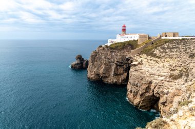 Cape Sao Vicente deniz feneri kayalık uçurumlarda, beyaz binalar ise bulutlu bir gökyüzünün altında, doğal renklerle tezat oluşturur..