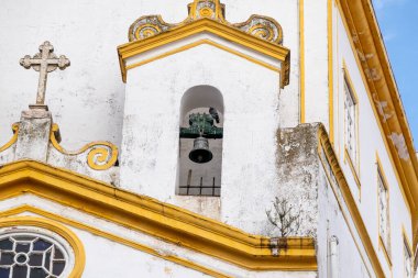 Close-up of Igreja da Misericordia bell tower with a bell, yellow decorative lines, cross on the gable, round window, dove, and cloudy sky. clipart