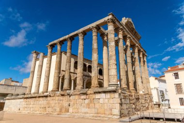 Merida 'daki Roma Tiyatrosu' nun yan manzarasında modern binalar ve mavi gökyüzü tarafından çerçevelenmiş Korint sütunları ve devasa taş bloklar yer almaktadır..