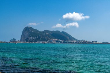 La Linea de la Concepcion sahil şeridinden Cebelitarık Kayası manzarası. Ön planda, turkuaz liman suyu ile şehir ve dağlar arka planda..