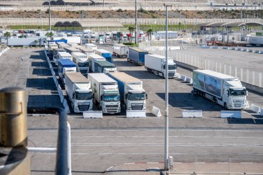 Tanger Med, Fahs-Anjra - Fas - 08-22-2024: Feribot terminali yakınlarında park yeri ve organize araçları olan liman; tepeler, binalar ve arkada mavi gökyüzü.