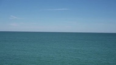 Cadiz, Cadiz - İspanya - 05-07-2024: Açık mavi gökyüzü altında büyük taş bloklar, alçak bir duvar ve renkli binalar ile denizden gezinti alanına Pan.