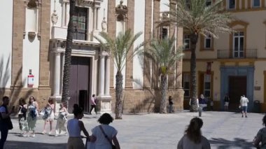 Cadiz, Cadiz - İspanya - 05-07-2024: Cadiz 'deki Via Augusta Kilisesi, beyaz unsurlu kahverengi taş cephe, süslü çan kulesi, haç, rüzgar gülü ve palmiye ağaçları.