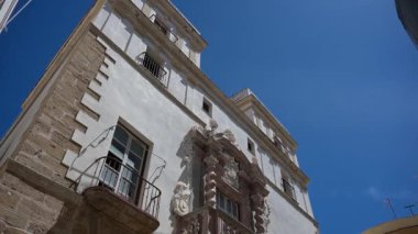 Cadiz, Cadiz - İspanya - 05-07-2024: Cadiz 'deki Amirallerin Evi' ne süslü cephe, sütunlar, balkon, kuleler, mücevher satan bir sokak satıcısı ve yakındaki binalar.