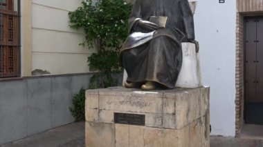 Cordobas Yahudi mahallesindeki Maimonides 'in bronz heykeli, kısmen parlak, güneşli, beyaz duvar ve arka planda çiçek açan sarmaşık..