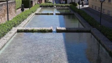 Cordoba, Cordoba - İspanya - 04-09-2024: Köpüklü su, kademeli kesitler, taş kenarlar, çalılar ve parlak bir güneş altında yaşayan insanların bulunduğu dikdörtgen çeşme.