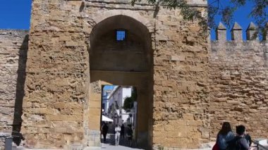Cordoba, Cordoba - İspanya - 04-09-2024: İnsanlar duvarlarında siperlerle ve yukarıda parlak mavi gökyüzüyle Cordoba şehir kapısından aşağı doğru yürürken,.