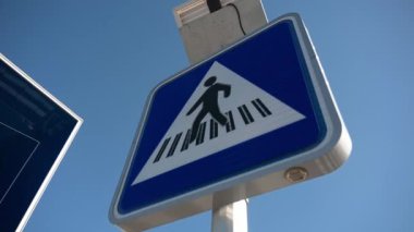 Işıkları yanıp sönen yaya geçidi tabelası güçlü rüzgarda belirgin bir şekilde sallanıyor. LED 'ler açık mavi gökyüzüne karşı yanıp sönmeye devam ediyor..