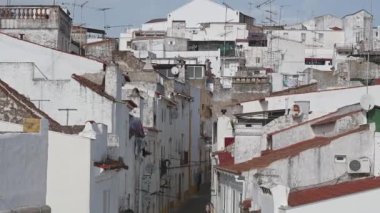 Elvas, Alentejo - Portekiz - 10-06-2024: Kırmızı kiremitli çatılar, beyaz boyanmış binalar, antenler ve mavi gökyüzü tarafından çerçevelenmiş dar sokaklar üzerinde soldan sağa doğru bir pan