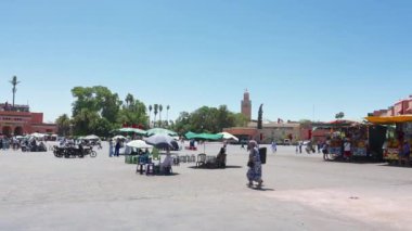 Marrakesch, Marrakesch-Safi - Fas - 08-14-2024: Marakeş 'te tezgahları, terasları, yeşil tenteleri ve parlak mavi gökyüzü altında alışveriş yapan müşterileri olan hareketli bir pazar meydanı.