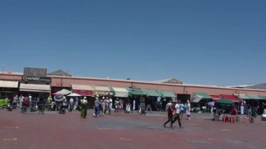 Marrakesch, Marrakesch-Safi - Fas - 08-14-2024: Renkli tezgahları, yeşil tenteleri, alışveriş merkezleri, terracotta binaları ve kameralar soldan sağa dönerken mavi gökyüzü.