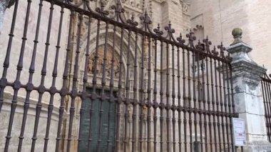 La Giralda 'dan Puerta de Palos' a doğru, ön planda güzel bir demir çit ve parlak mavi-beyaz bir gökyüzü tarafından çerçevelenmiş..