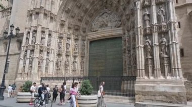 Sevilla, Sevilla - İspanya - 04-19-2024: Güneş ışığı üzerinde aşağıdan yukarıya, sanatsal Puerta de la Asuncion; heykeller ve oymalar; insanlar hafifçe si ye yürüyorlar