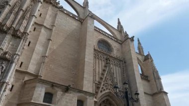 Seville Katedrali 'nin üst batı cephesinde sağdan sola kaydır; Puerta de la Asuncion' da sona erer; ince bulutlu mavi gökyüzü.