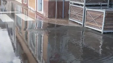 Su, su basmış bir sokaktan başka bir yola akıyor. Su, su yüzeyine hızla yayıldıkça, su altında kalan ahşap parçaları topluyor..