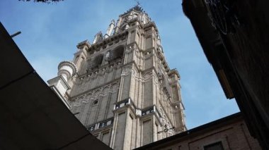 Gölgelerle çerçevelenmiş Toledo Katedrali 'nin çan kulesine dar bir sokaktan bak. Mavi gökyüzüne karşı detaylı mimarisini sergiliyor.