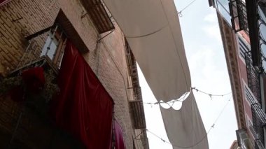 Toledo, Toledo - İspanya - 06-05-2024: Uzun, pamuk renkli bir kumaş dar bir sokakta asılı duruyor, kumaş boyunca ilerleyip manzaranın sonunda tarihi bir kilise girişine doğru ilerliyor.