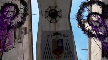 Toledo, Toledo - İspanya - 06-05-2024: Bir Toledo geçidinde kumaş paneller boyunca dönmek, sağda katedral ve solda başpiskoposluk, çelenklerle süslenmiş ve ben