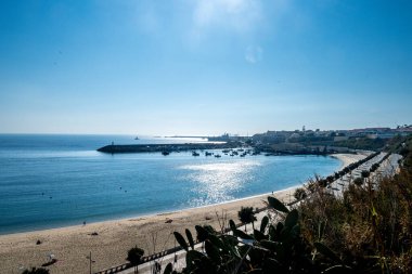 Güneş ışığını yansıtan sahil gezintisi, sakin deniz, köstebeğin yakınındaki tekneler, arka planda evleri ve liman bölgesi olan..