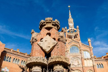 Sant Pau 'nun önünde haç amblemi olan dekoratif tuğla bir yapı, taş detayları ve sanatsal mimariyi vurguluyor..