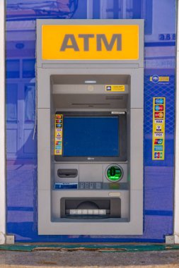 Mavi çerçeve ve kart sembolleriyle çevrili sarı ATM işaretli modern bir ATM 'nin yakın çekimi..