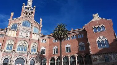 Barselona, Katalonya - İspanya - 01-08-2025: Kemerli camları, dekoratif heykelleri, mozaikleri ve açık mavi gökyüzü altındaki palmiye ağaçlarıyla Sant Paus 'un sağdan sola doğru uzanan kırmızı tuğla cephesi.