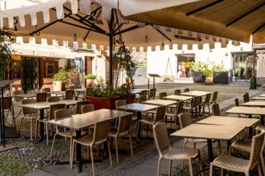 Alghero, Sardinia - İtalya - 02-13-2025: Alghero, Sardinya 'da masa ve sandalyeli boş bir kafeterya. Bej tenteler gölge sağlar. Dükkanlar ve bitkiler sıcak bir ortam yaratır..