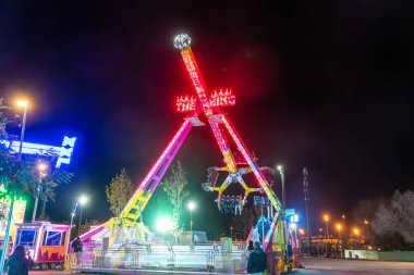 Barselona, Katalonya - İspanya - 01-07-2025: Aydınlatılmış lunapark gezisi Gece Kral, kırmızı ve sarı ışıklar ve sallanan yüksek binalı yolcular.
