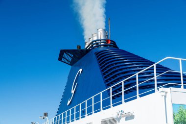 Barselona, Katalonya - İspanya - 01-10-2025: Grimaldi Cruise Roma feribot hunisinin altından beyaz duman, metal korkuluklar, güverte ışıkları ve mavi gökyüzüne karşı havalandırma boruları.