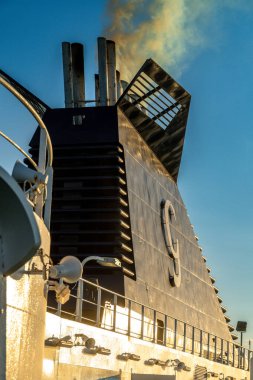 Barselona, Katalonya - İspanya - 01-10-2025: Gün batımında soluk bir gökyüzüne metal korkuluklar ve lambalarla soluk duman saçan büyük siyah bir gemi bacasının yakın çekimi.
