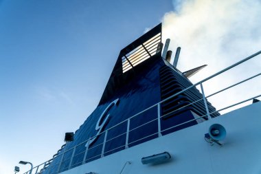 Barselona, Katalonya - İspanya - 01-10-2025: Grimaldi Cruise Roma feribot hunisinin altından beyaz duman, metal korkuluklar, güverte ışıkları ve mavi gökyüzüne karşı havalandırma boruları.
