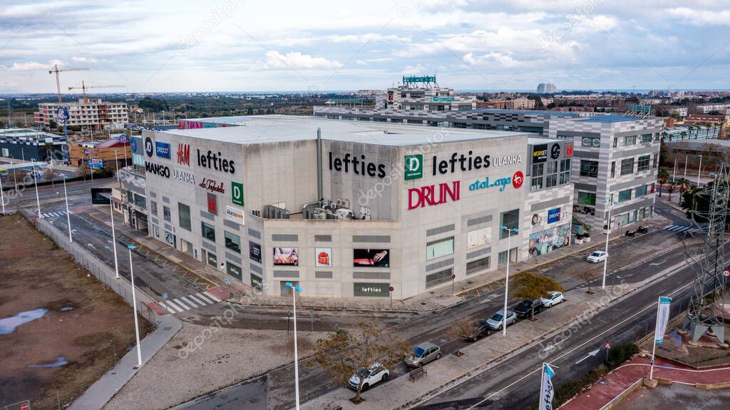 Puerto de Sagunto - Valencian Community - Spain- 01-01-2025: Large shopping mall in Sagunt with multiple brand logos displayed on its facade, surrounded by empty streets and a partly cloudy sky.