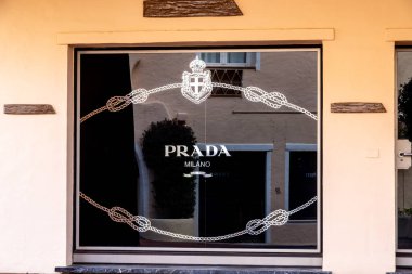 Porto Cervo - Sardinien - Italien - 02-22-2025: Prada Milano logosu siyah bir vitrinde dekoratif zincir tasarımlı, Porto Cervo, Sardinya, İtalya 'daki yakın mimariyi yansıtıyor.