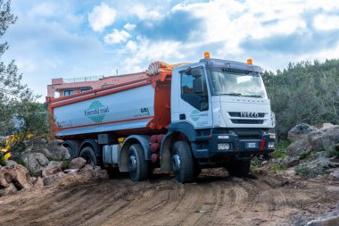 Porto Cervo - Sardinien - Italien - 02-22-2025: Zümrüt Yolu markalı Iveco damperli kamyon Porto Cervo, Sardunya 'da, kayalar ve ağaçlarla çevrili engebeli inşaat sahasında.