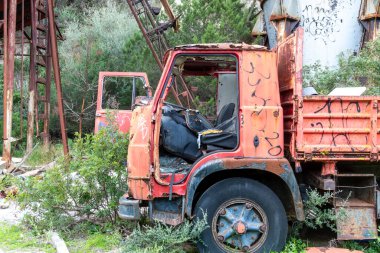Golfo Aranci - Sardinien - Italien - 02-24-2025: Aşırı gelişmiş sanayi kireç donanımının yanında parçalanmış iç ve pas gösteren ağır hasar görmüş kırmızı bir kamyonun ayrıntılı görüntüsü.