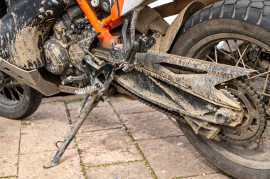 Bosa - Sardinien - Italien - 02-28-2025: Çamurlu zincir, çıkıntı, tekmeleme, ayaklık ve lastik içeren kirli motosiklet arka kısmının ayrıntılı görüntüsü.