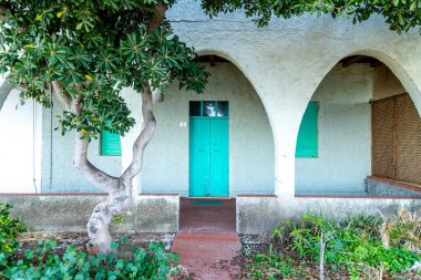 SArchittu - Sardinien - Italien - 03-02-2025: Yeşil kapılı, yeşil panjurlu, beyaz kemerli ve Schittu, Sardinya, İtalya 'da ön planda bir ağaç.