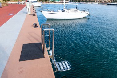 Porto Cervo - Sardinien - Italien - 02-22-2025: Sardinya 'nın Porto Cervo kentindeki beton iskeleden suya uzanan paslanmaz çelik marina merdiveni.